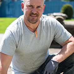man squatting with arm resting on leg staring into camera